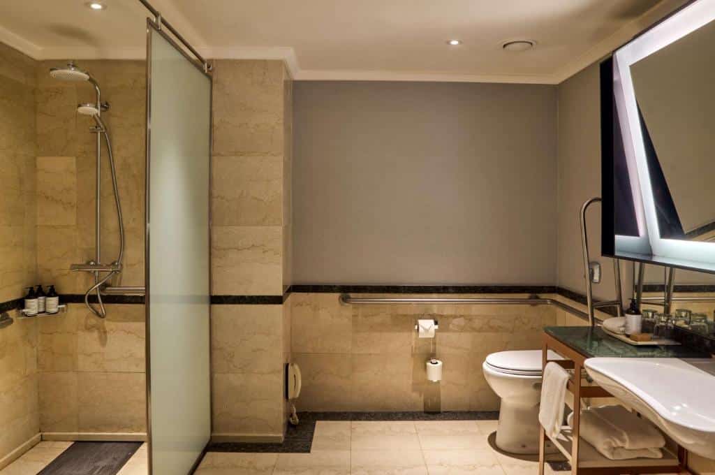 banheiro do Hilton Buenos Aires com adaptações como barras de apoio no vaso sanitário e no box aberto, com chuveirinho e pia com espaço aberto