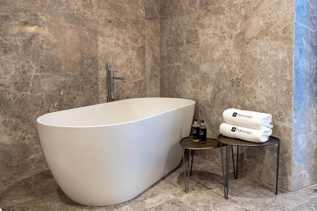 Banheira oval no banheiro de um dos quartos do Boemio FLH Hotels com duas mesinhas ao lado com toalhas e produtos de higiene