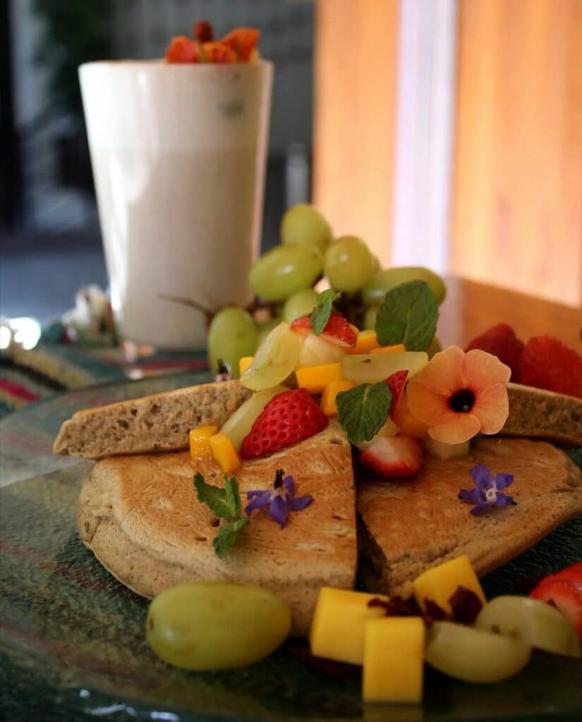 prato de panquecas doces com frutas diversas e um copo alto de vitamina ao fundo para representar o cardápio do Organika Bakery & Coffee, um dos lugares onde comer em Cusco