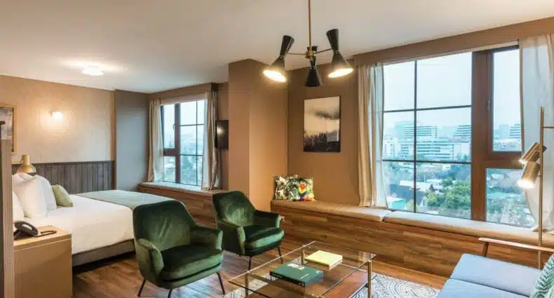 Quarto do Hotel Eco Boutique Bidasoa com sala de estar do lado direito da imagem com uma mesa de centro e duas cadeiras a frente e no fundo uma cama de casal. Representa hotéis para família em Santiago.