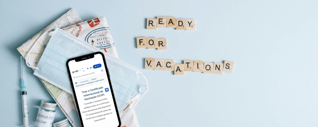 Um celular com o site do gov.br aberto, há também um máscara descartável, uma seringa e alguns documentos sob a mesa