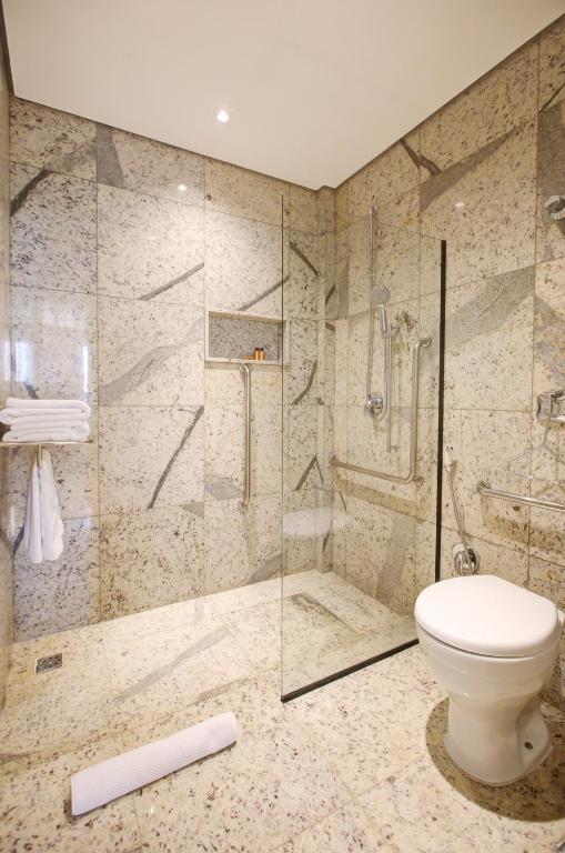 Banheiro do DoubleTree by Hilton que mostra do lado direito um vaso sanitário com barras de apoio e ao fundo o box de vidro com uma espaço aberto e dentro algumas barras de apoio perto do chuveiro. Imagem ilustrando post Resorts em Foz do Iguaçu.