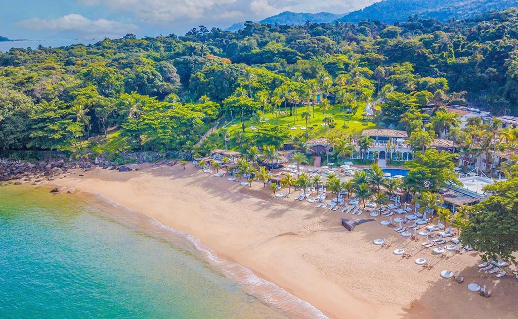 Foto aérea do DPNY Beach Hotel & Spa llhabela. Na esquerda está o mar, e na direita vemos a areia e a estrutura do hotel. Também há muitas árvores e áreas verdes.