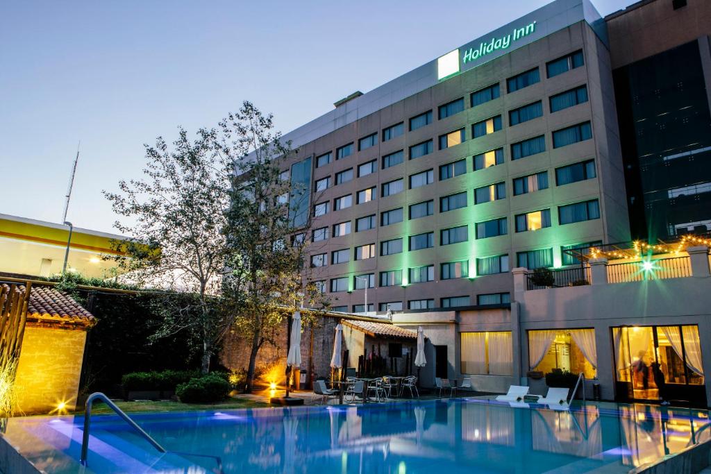 fachada do Holiday Inn Ezeiza Airport, an IHG Hotel, um dos hotéis perto do aeroporto em Buenos Aires, com as janelinhas em tons de azul e piscina abaixo iluminada