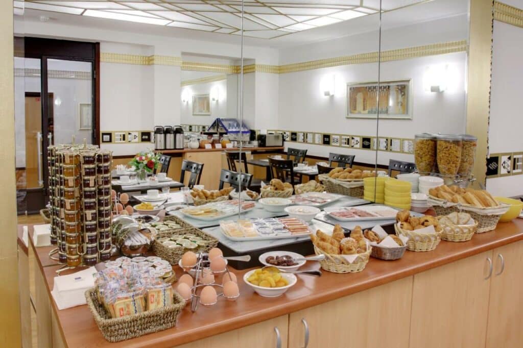 Bancada com vários itens de café da manhã no Hotel Opéra d'Antin, como pães, frios, cereais e ovos. Um espelho logo acima reflete mesas de refeição dispostas no local.