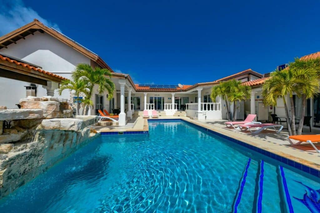 Uma das piscinas do Boutique Hotel Swiss Paradise Aruba Villas and Suites. Ela é grande e está em uma área aberta, cercada por espreguiçadeiras e pelo próprio hotel. Essa é uma das melhores opções de hotéis baratos em Aruba.