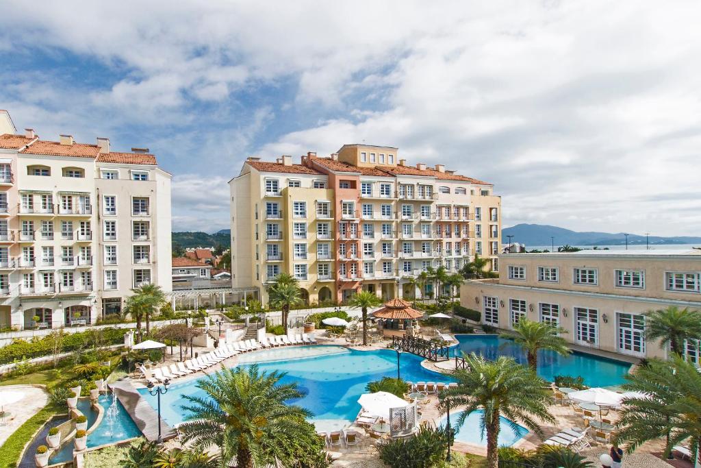 IL Camparino Villaggio Resort em Florianópolis com vários andares com varandas com vista para uma piscina externa, palmeiras e espreguiçadeiras sob um céu parcialmente nublado.
