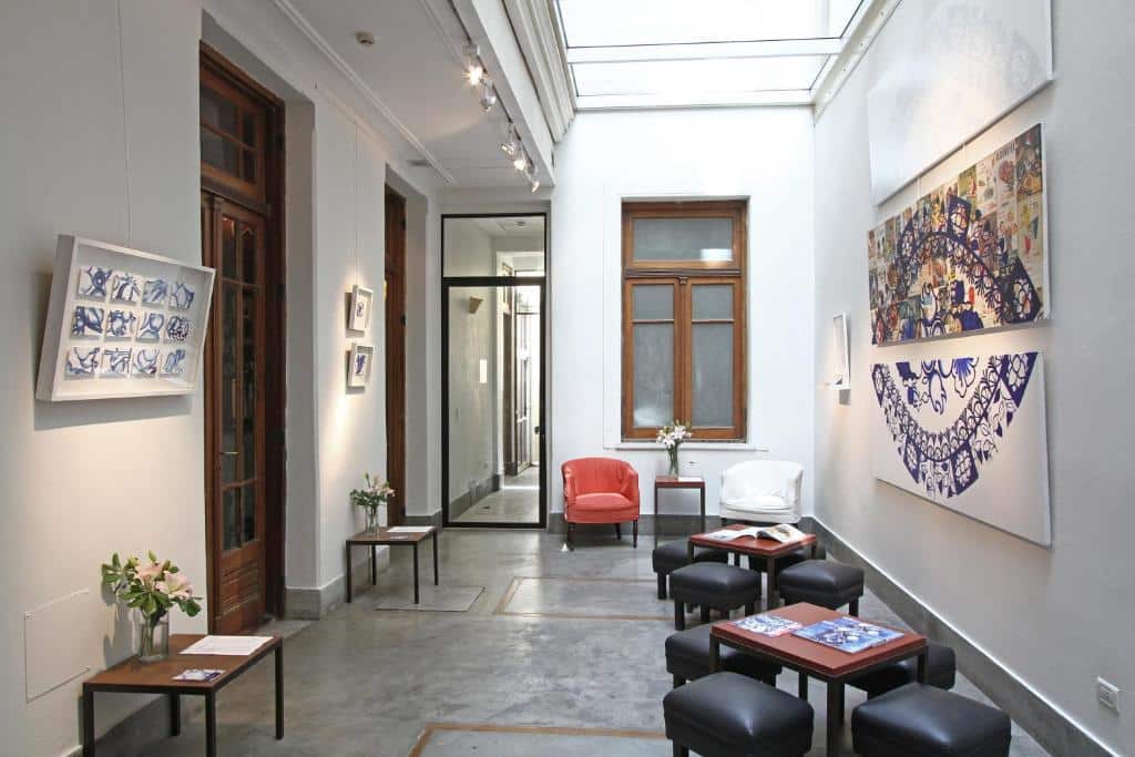 lounge do A Hotel, um dos hotéis 3 estrelas em Buenos Aires, com banquinhos acolchoados, mesas baixas, poltronas, quadros na parede e portas de madeira e vidro