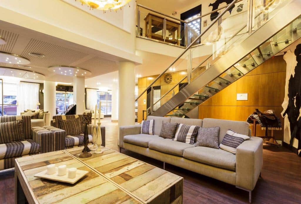 lounge do Hotel Facon Grande um dos hotéis 3 estrelas em Buenos Aires com mesa de centro de madeira, sofá comprido, escada que leva para um segundo andar cheio de quadros e mais decorações com padronagem de vaca