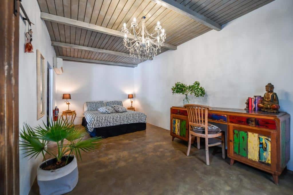 Quarto do B&B Mammaloe. Uma cama de casal está ao fundo, entre dois abajures. Na frente dela, encostada na parede direira está uma mesa com cadeira. Na parede esquerda há uma planta e um quadro.