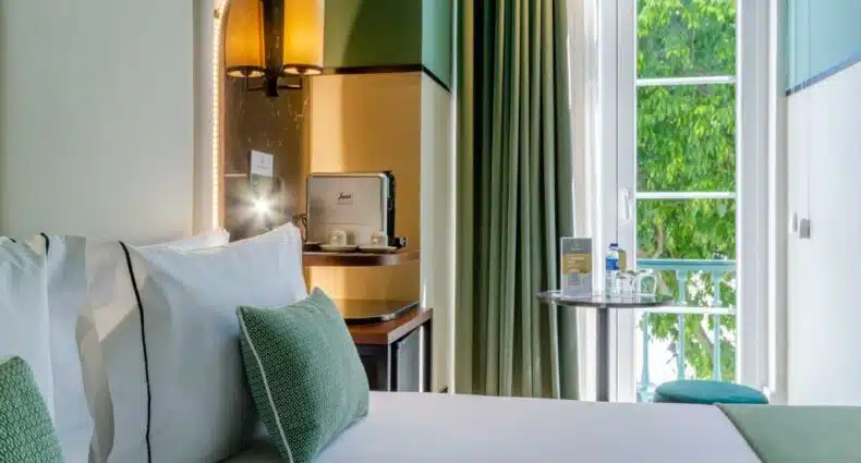 Quarto do Nicola Rossio Hotel com uma cama de casal e, ao lado dela, há uma sacada de vidro com vista para as árvores da Praça do Rossio em Lisboa