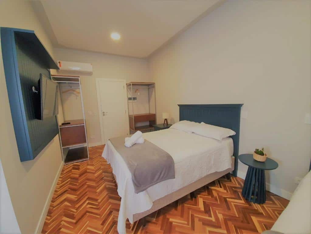 Quarto da Paranaguá Lodge. Uma cama de casal do lado direito com uma mesinha de apoio de cada lado, de frente uma televisão. No fundo um ar-condicionado e dois closets abertos. Foto para ilustrar post sobre pousadas pet friendly no Paraná.