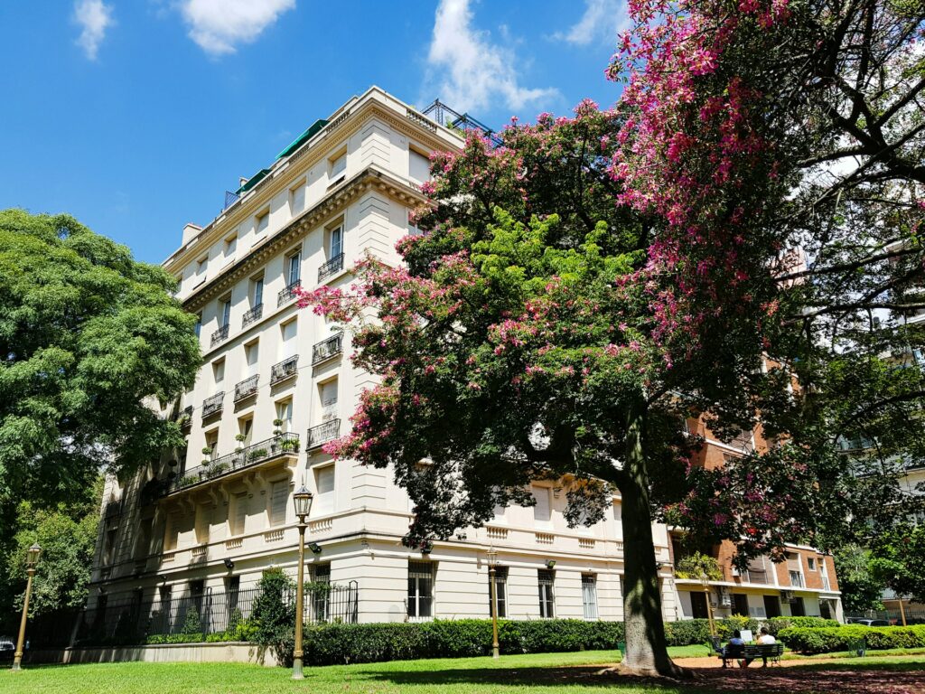 vista de um prédio histórico com fachada clara e bastante detalhada com árvores floridas ao redor e grama abaixo no Parque Recoleta, em Buenos Aires