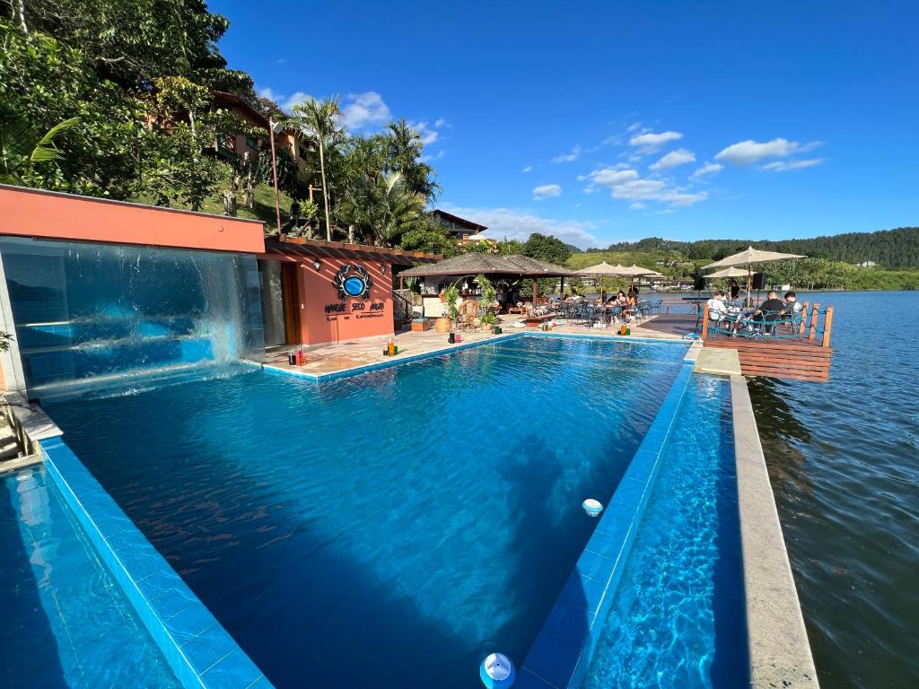 piscina de borda infinita com cascata e deck com várias mesinhas e cadeiras no Pousada e Restaurante Mangue Seco Angra