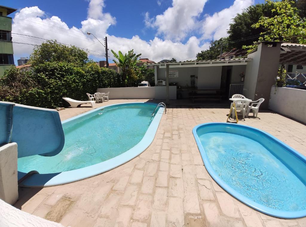 Duas piscinas externas no Hotel D'Luz, uma das pousadas em Itapema, uma com escorregador, cercadas por cadeiras e vegetação sob um céu parcialmente nublado.