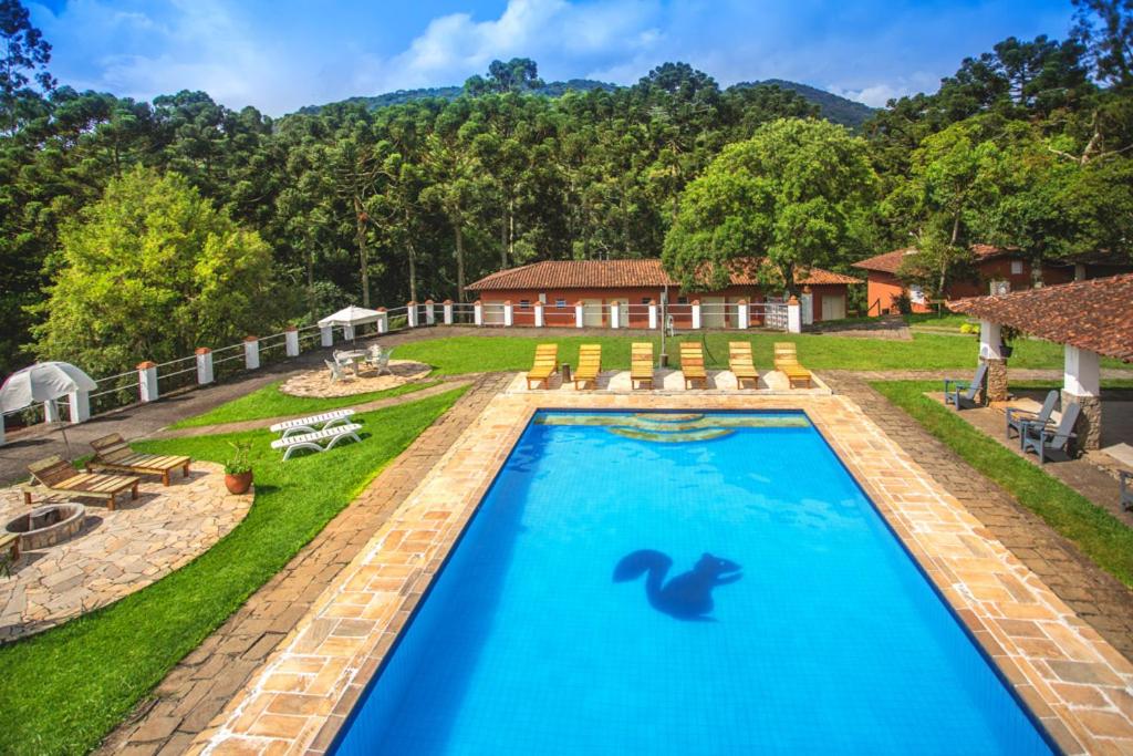Área externa da Pousada Águas do Vale. Uma piscina no meio, ao redor o jardim, vista das montanhas e cadeiras de tomar sol.