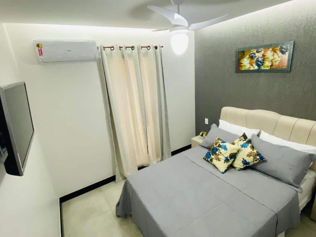 Quarto da Pousada Amaral Búzios. Uma cama de casal do lado direito, do lado esquerdo uma televisão, no fundo uma cortina.