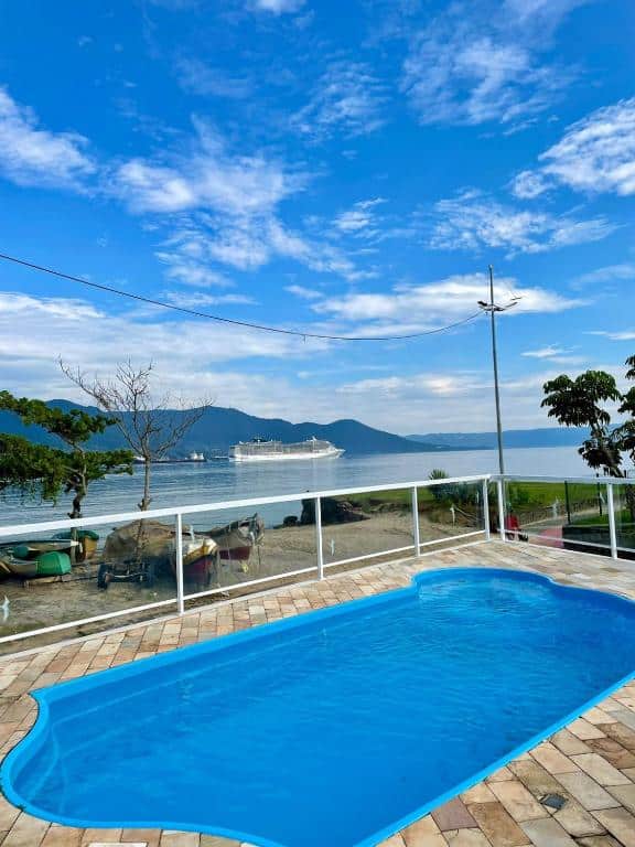 Exterior da Pousada Bonns Ventos com piscina em um deck de pedra. Além da piscina, há uma vista para o mar.
