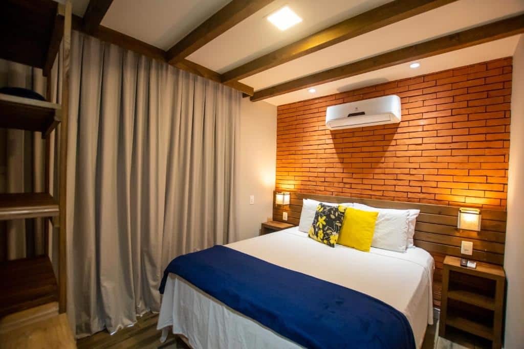 Quarto da Pousada Cacau. Uma cama de casal, de cada lado uma cômoda com luminária, em cima um ar-condicionado. Foto para ilustrar post sobre pousadas pet friedly em Santa Catarina.