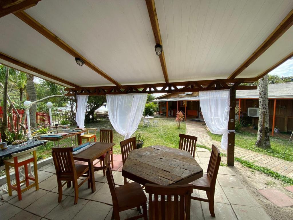 Área externa da Pousada Cantuá. Mesas e cadeiras de madeira numa área coberta, ao redor grama.