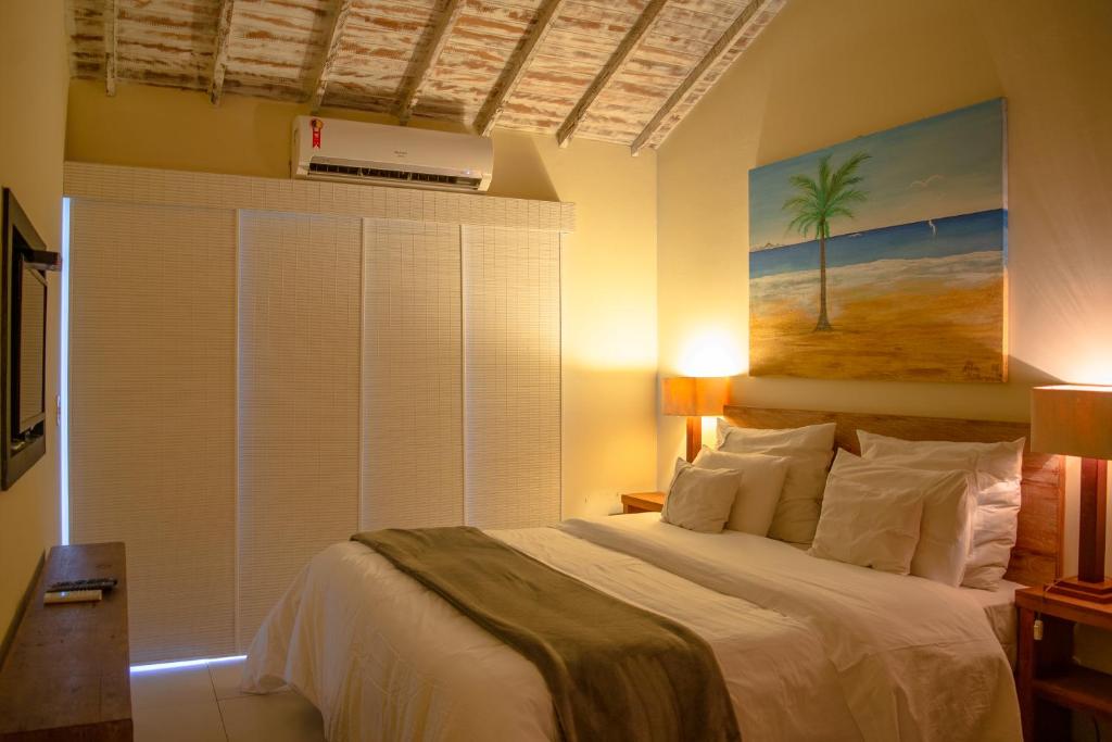 Quarto da Pousada da Cyssa. Do lado direito uma cama de casal, de cada lado uma mesinha de apoio com abajur. Do lado esquerdo uma estante, uma televisão. No fundo a cortina e o ar-condicionado. Foto para ilustrar post sobre pousadas pet friendly em Búzios.