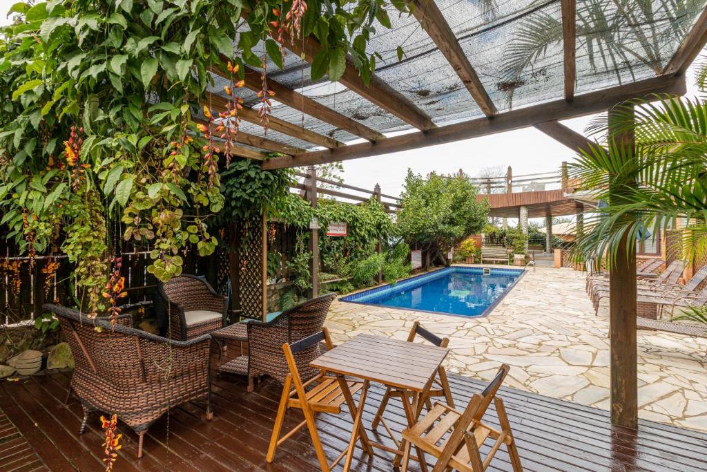 Área externa da Pousada Descanso do Rei. Uma piscina no fundo no meio, do lado direito cadeiras de tomar sol. Na parte da frente um deck de madeira com cadeiras e mesas.