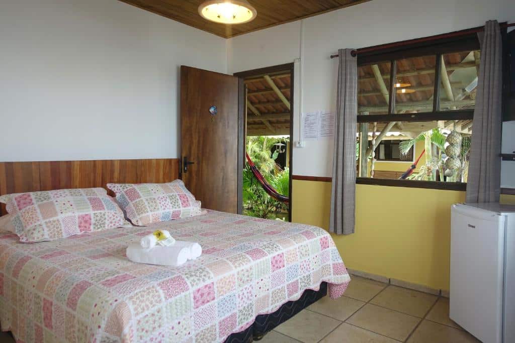Quarto da Pousada La Luna - Frente Mar. Uma cama de casal do lado esquerdo, de frente um frigobar. No fundo a porta do quarto e uma janela. Foto para ilustrar post sobre pousadas pet friedly em Santa Catarina.