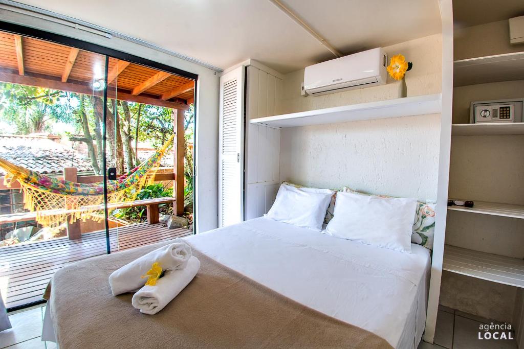 Quarto da Pousada Rosa. Uma cama de casal no cento, do lado direito prateleiras, em cima da cama um ar-condicionado, do lado esquerdo do quarto uma varanda com rede. Foto para ilustrar post sobre pousadas pet friedly em Santa Catarina.
