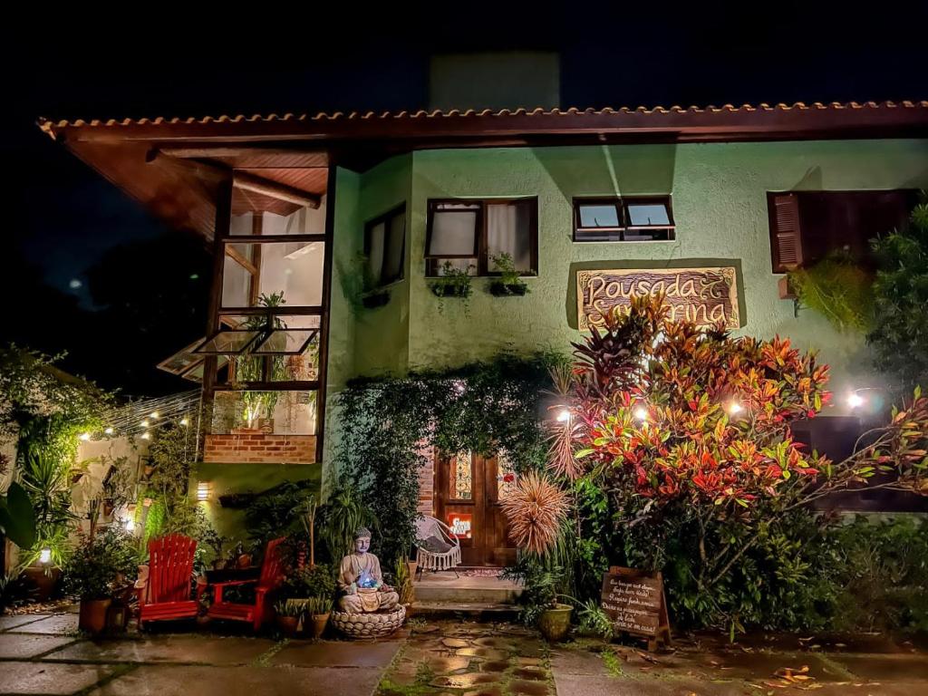 Foto tirada à noite da Pousada Santarina. Mostra a construção externa da casa, sua fachada e um jardim bastante cheio e iluminado.
