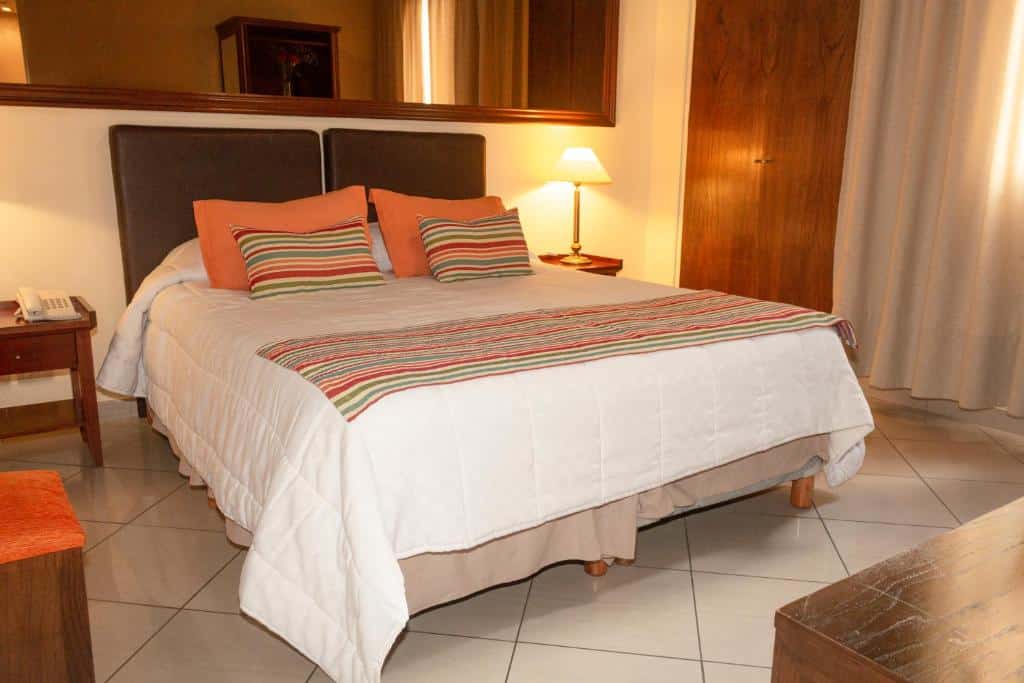 quarto do O2 Hotel Buenos Aires com cama de casal, mesinha e luminária de ambos os lados, espelho acima e poltronas com mesa do lado
