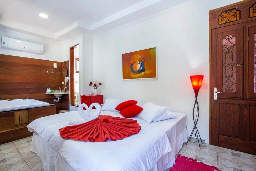 Quarto romãntico da  Pousada Vila Barequeçaba com uma cama de casal e uma banheira de hidromassagem do lado esquerdo, a decoração conta com itens vermelhas e rústicos