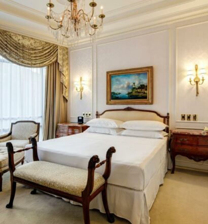 Imagem do Sheraton Santiago Hotel & Convention Center com cama de casal no centro do quarto com uma comoda em cada lado com um banco estofado do pé da cama. Representa hotéis 5 estrelas em Santiago.