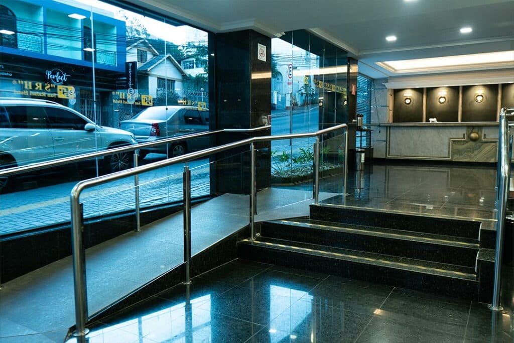 Hotel San Rafael Comfort Class, em Foz do Iguaçu, que possui uma rampa de acesso para que pessoas com cadeira de rodas possam adentrar o hall do hotel. A rampa está na esquerda, e uma escada está do seu lado à direita.