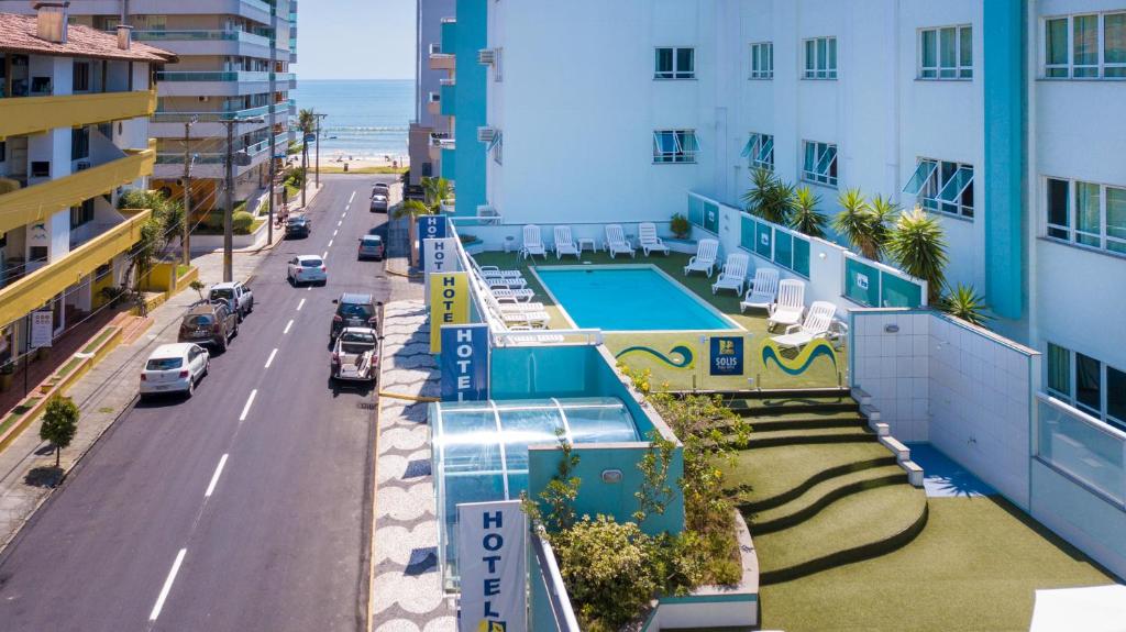 Solis Praia Hotel Itapema com uma piscina externa e espreguiçadeiras está localizado próximo a uma rua, com a praia visível ao fundo.