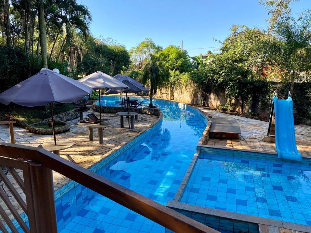 Parte do Suíça Hotel & Resort que mostra a piscina ao ar livre em formato de túnel e um escorregador do lado direito. Do lado esquerdo tem umas mesinhas com guarda-sóis. Imagem ilustrando post Resorts em Foz do Iguaçu.
