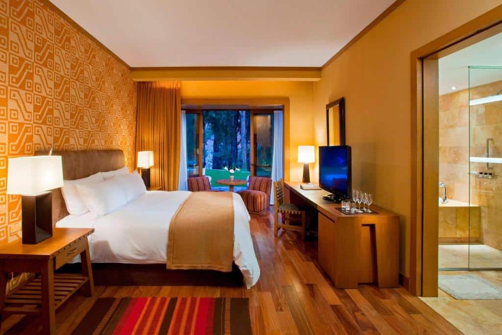 Suíte do Tambo del Inka, a Luxury Collection Resort & Spa, Valle Sagrado com uma cama de casal à esquerda do quarto, uma varanda com portas duplas que dão acesso ao jardim e uma porta à direita que dá acesso ao banheiro com banheira, para representar hotéis no Vale Sagrado dos Incas.