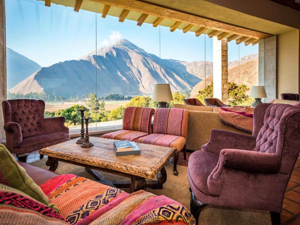 Lounge compartilhado do Inkaterra Hacienda Urubamba com vista para as montanhas peruanas do Vale Sagrado dos Incas. O espaço conta com várias poltronas e sofás com estampas étnicas.
