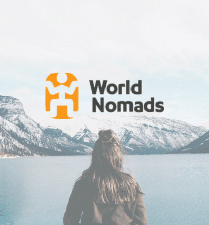 Uma mulher parada em frente a um grande lago com montanhas nevadas ao fundo, para representar seguro viagem da World Nomads