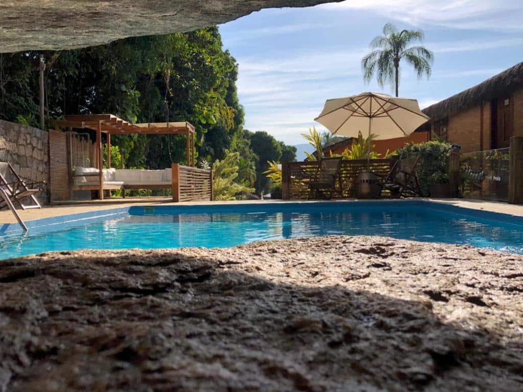 Foto do Yannai Chalé Praia, mostrando uma piscina e deck com quiosque, mesa, espreguiçadeira e guarda-sol.