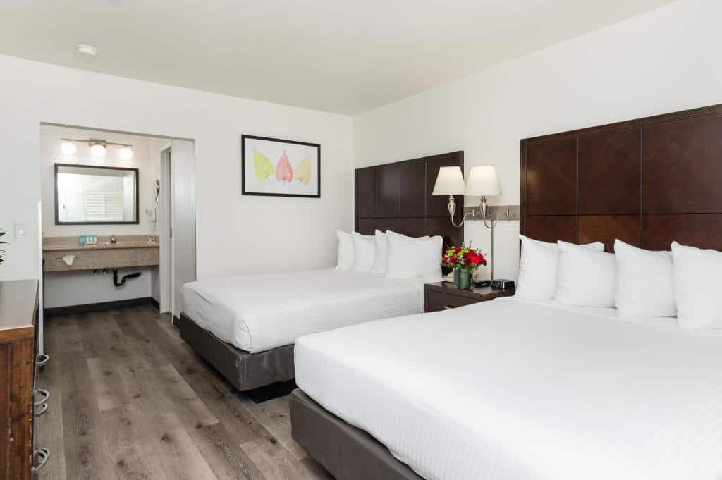 Quarto do Alpine Inn near Convention Center and the Park. Duas camas de casal do lado direito, entre elas uma cômoda e um abajur. Do lado esquerdo uma cômoda, no fundo um espelho e a pia do banheiro.