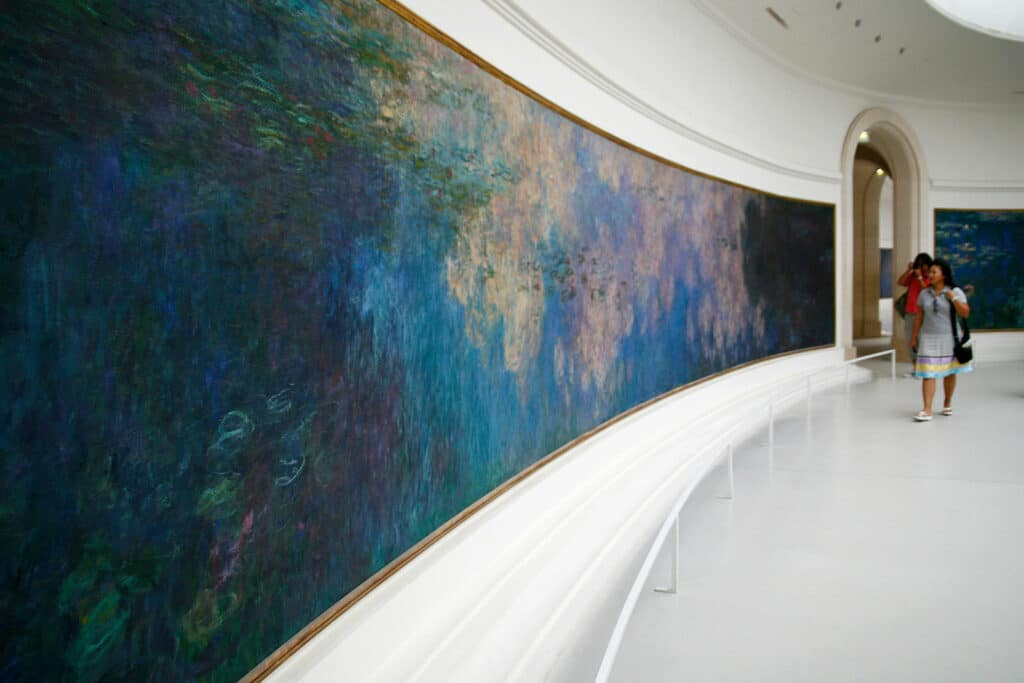 Duas mulheres vendo um quadro impressionista no Museu l'Orangerie, uma das opções de o que fazer em Paris. O quadro ocupa a parede toda.