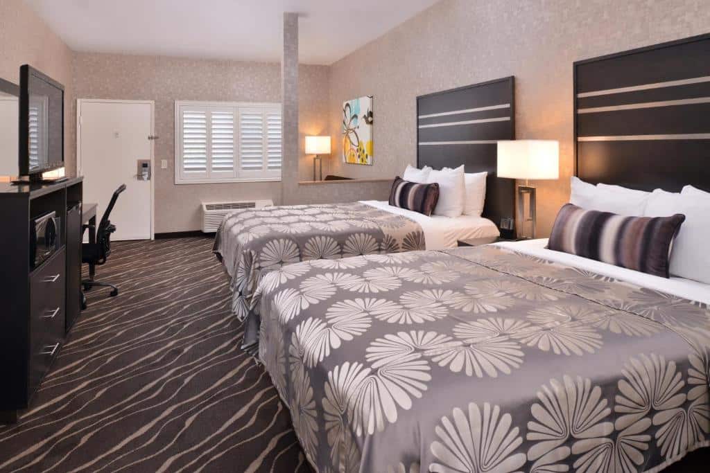 Quarto do Best Western Plus Park Place Inn. Duas camas de casal do lado direito, do lado esquerdo uma cômoda, uma televisão e uma mesa de trabalho.