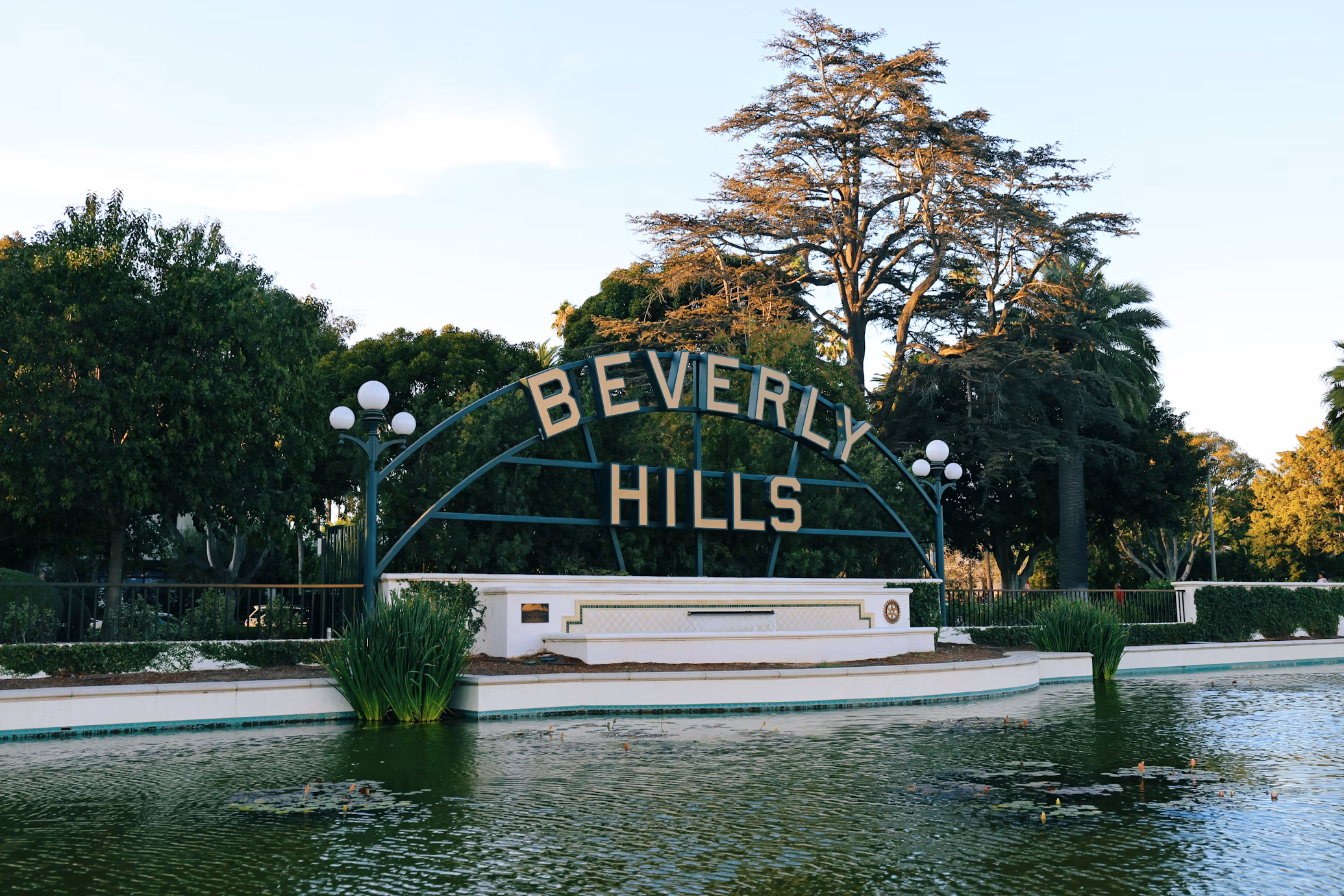 Placa de Beverly Hills dentro de uma fonte de água. Atrás dela estão várias árvores.