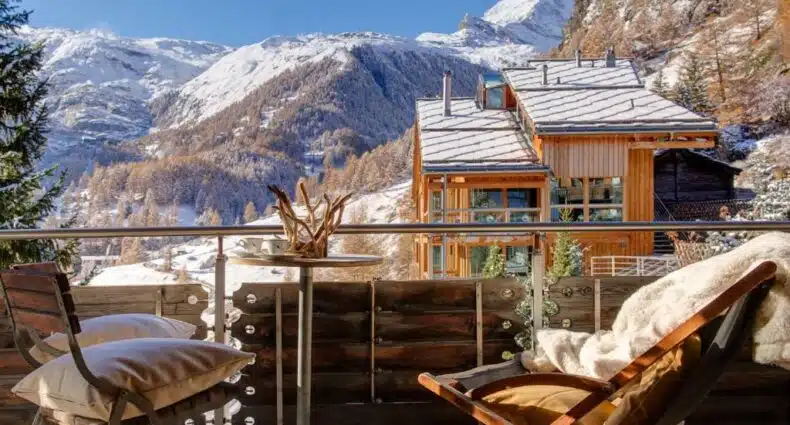 Varanda do Backstage Hotel Serviced Apartments durante o dia com duas cadeiras de cada lado e no meio uma mesa redonda com vista para as montanhas. Representa onde ficar em Zermatt.