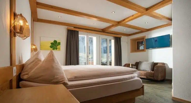 Quarto do Hotel Silberhorn com cama de casal do lado esquerdo da imagem, em frente a cama um sofá com uma TV em cima. Representa hotéis em Lauterbrunnen.