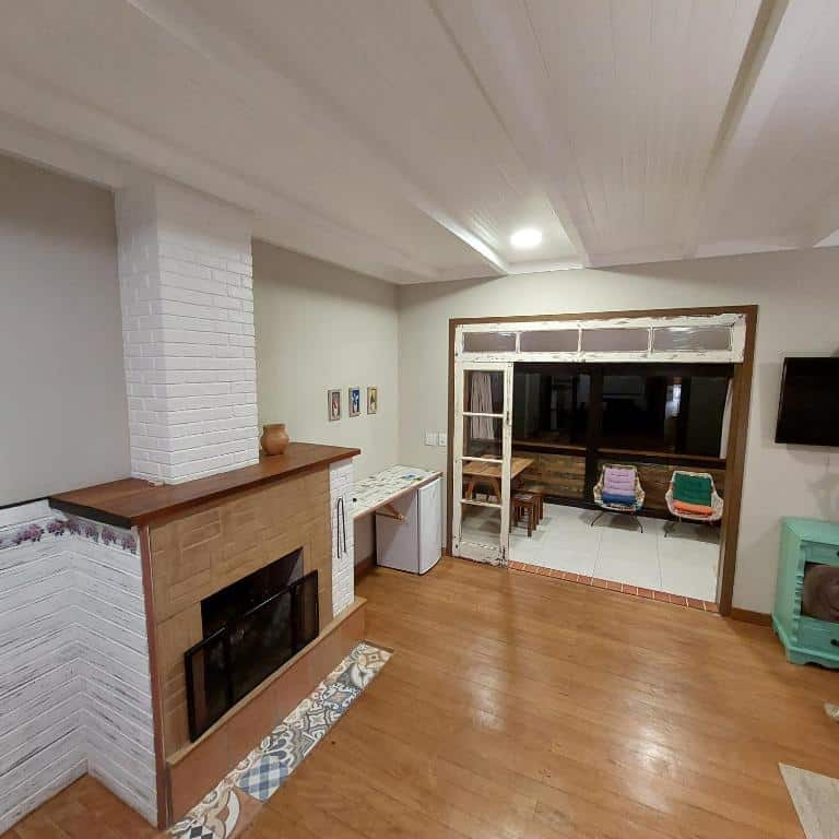 Sala de estar da Casa no Céu com uma lareira do lado esuqerdo, piso de madeira e uma porta aberta que leva a uma sala de estar com cadeiras e uma mesa.