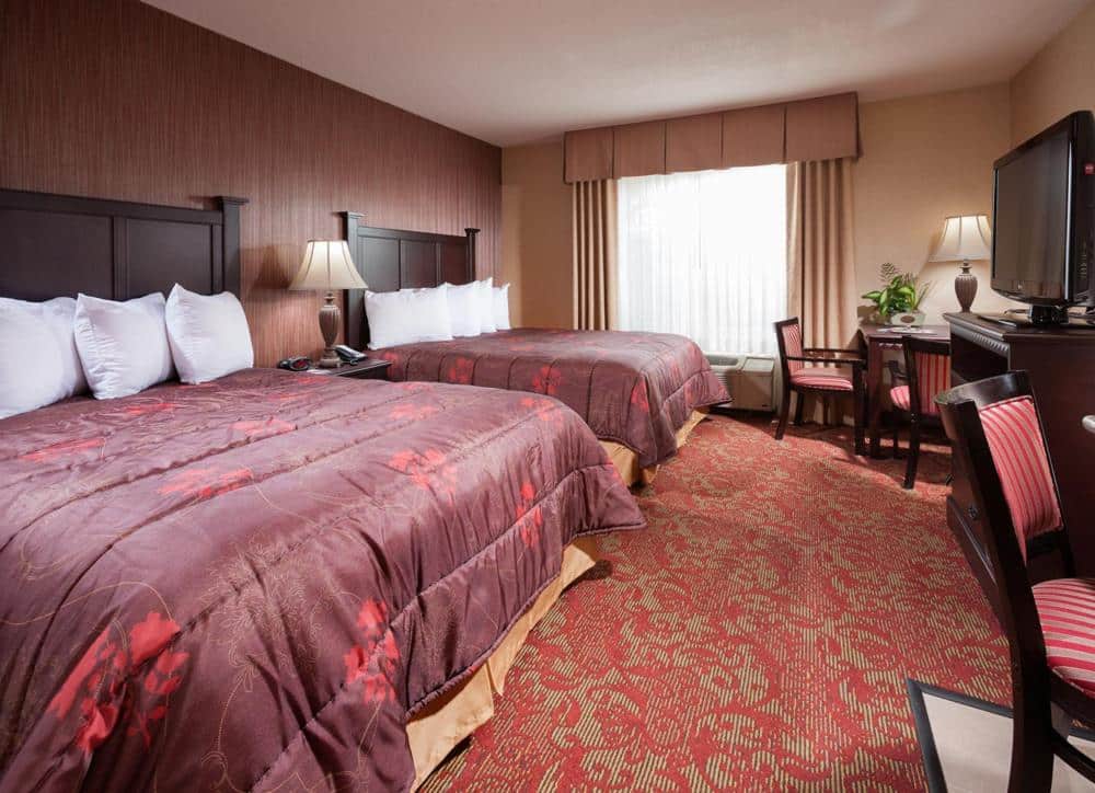 Quarto do Castle Inn and Suites Anaheim. Duas camas de casal do lado esquerdo, entre elas uma cômoda com abajur. Do lado direito uma mesa com cadeiras e uma cômoda com televisão.