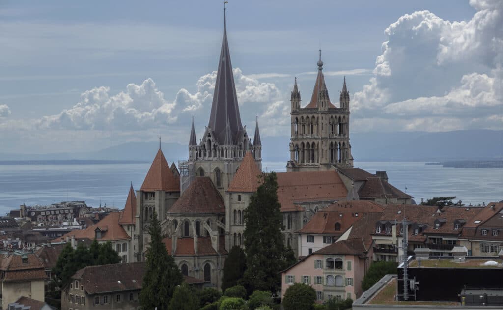 Imagem da Catedral de Lausana durante o dia com a catedral no centro em volta de casas antigas. Representa o que fazer em Lausanne na Suíça.