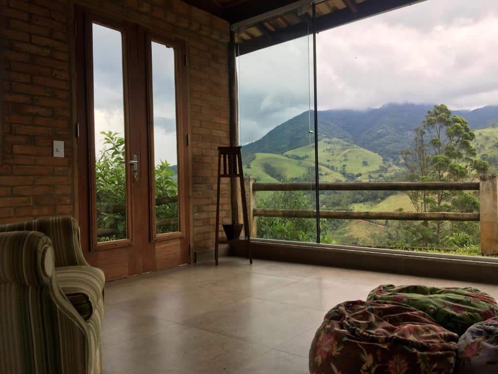 Vista do Chalés de Valfena. Uma grande janela de vidro em um cômodo mostra a vista das motanhas e das árvores.