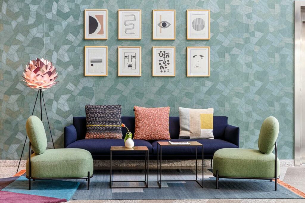 Sala de estar de um dos apartamentos do Citadines Sloterdijk, um dos aluguel de temporada em Amsterdam, com um sofá azul no meio com almofadas no tom rosa, azul, branco e amarelo em cima, duas poltronas verdes á frente e, entre elas, há duas mesinhas de centro. A parede possui quadros no mesmo tom